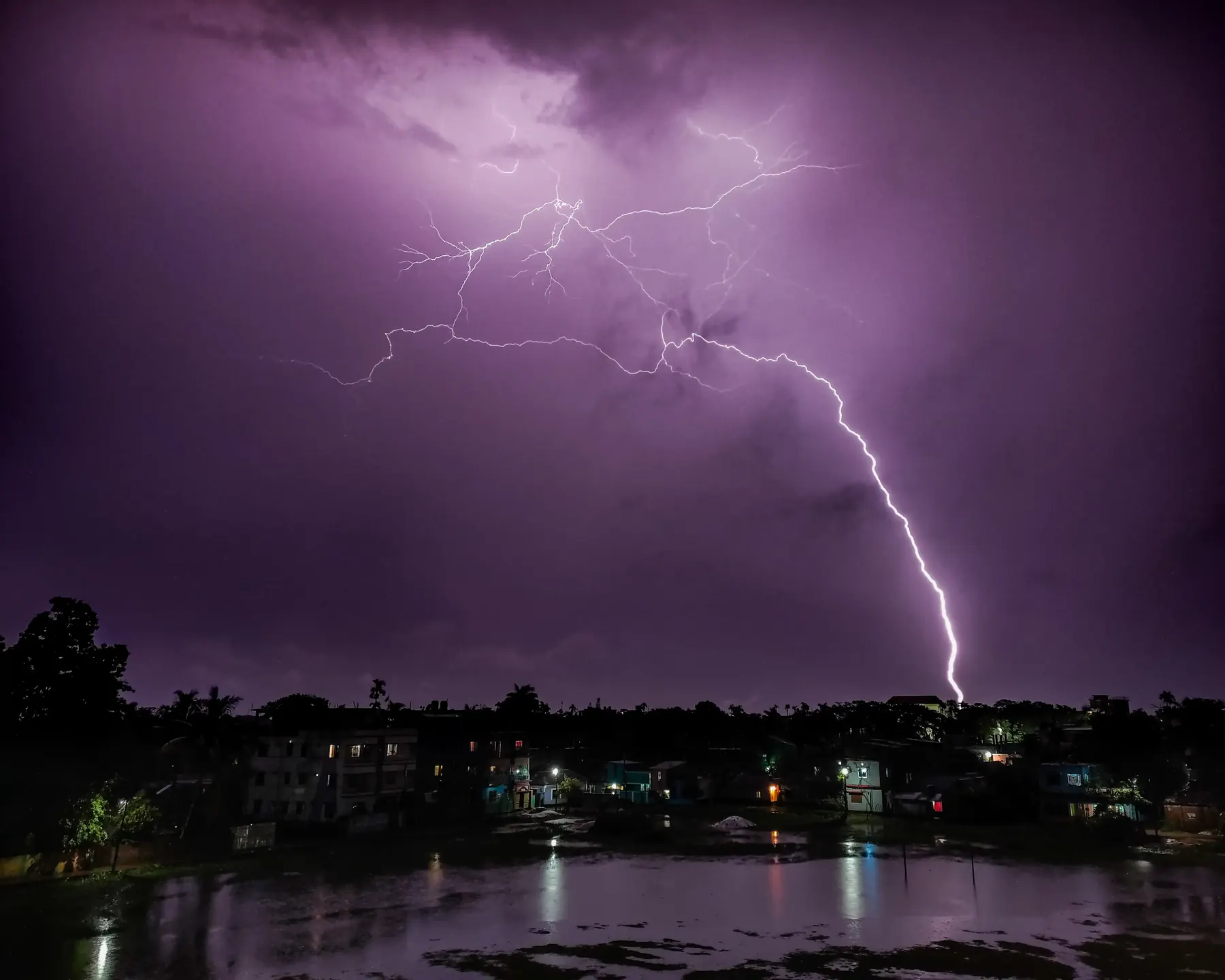 Purple lightning striking over a city skyline and river