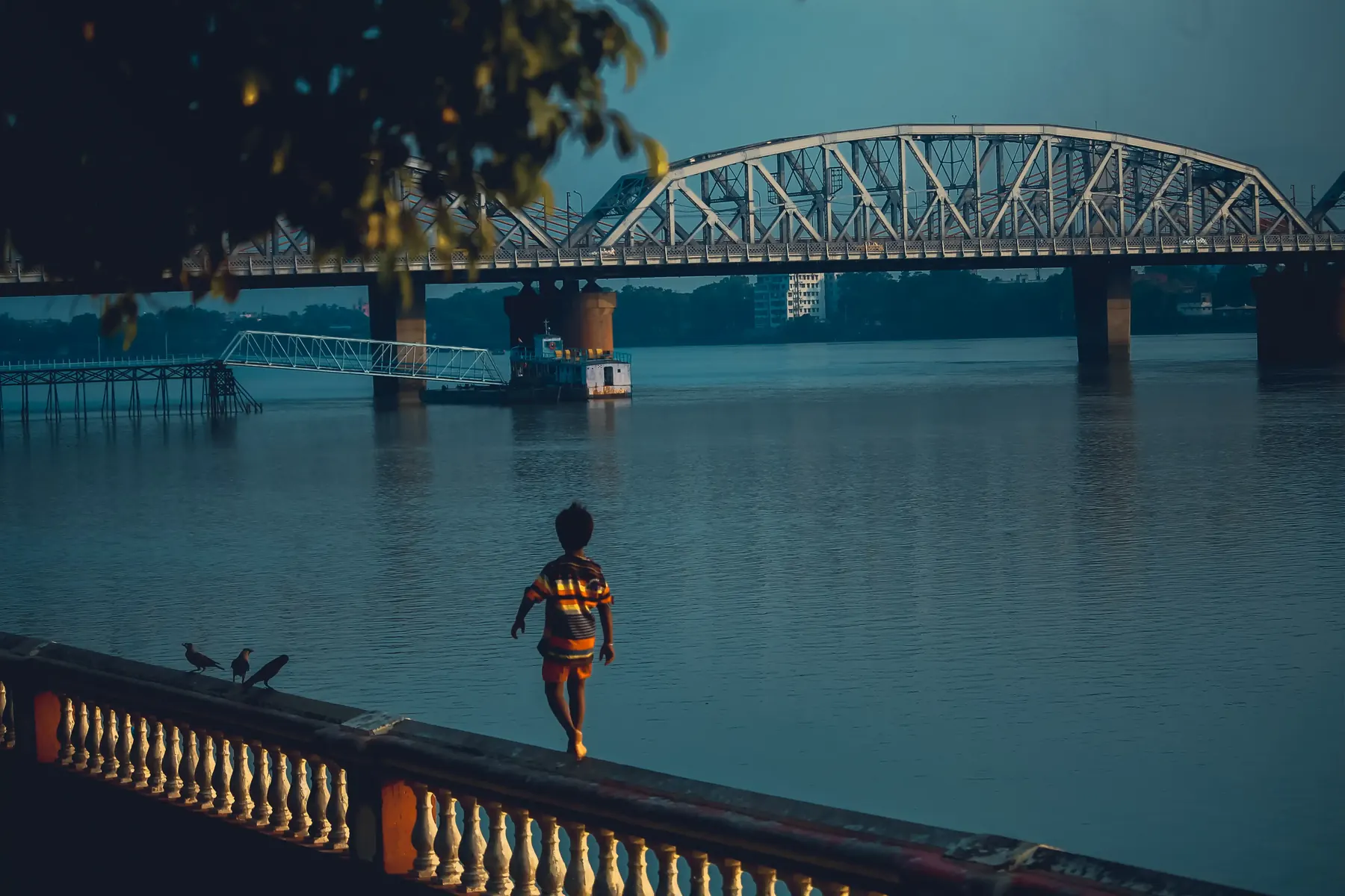 A person walking across a river bridge at blue hour