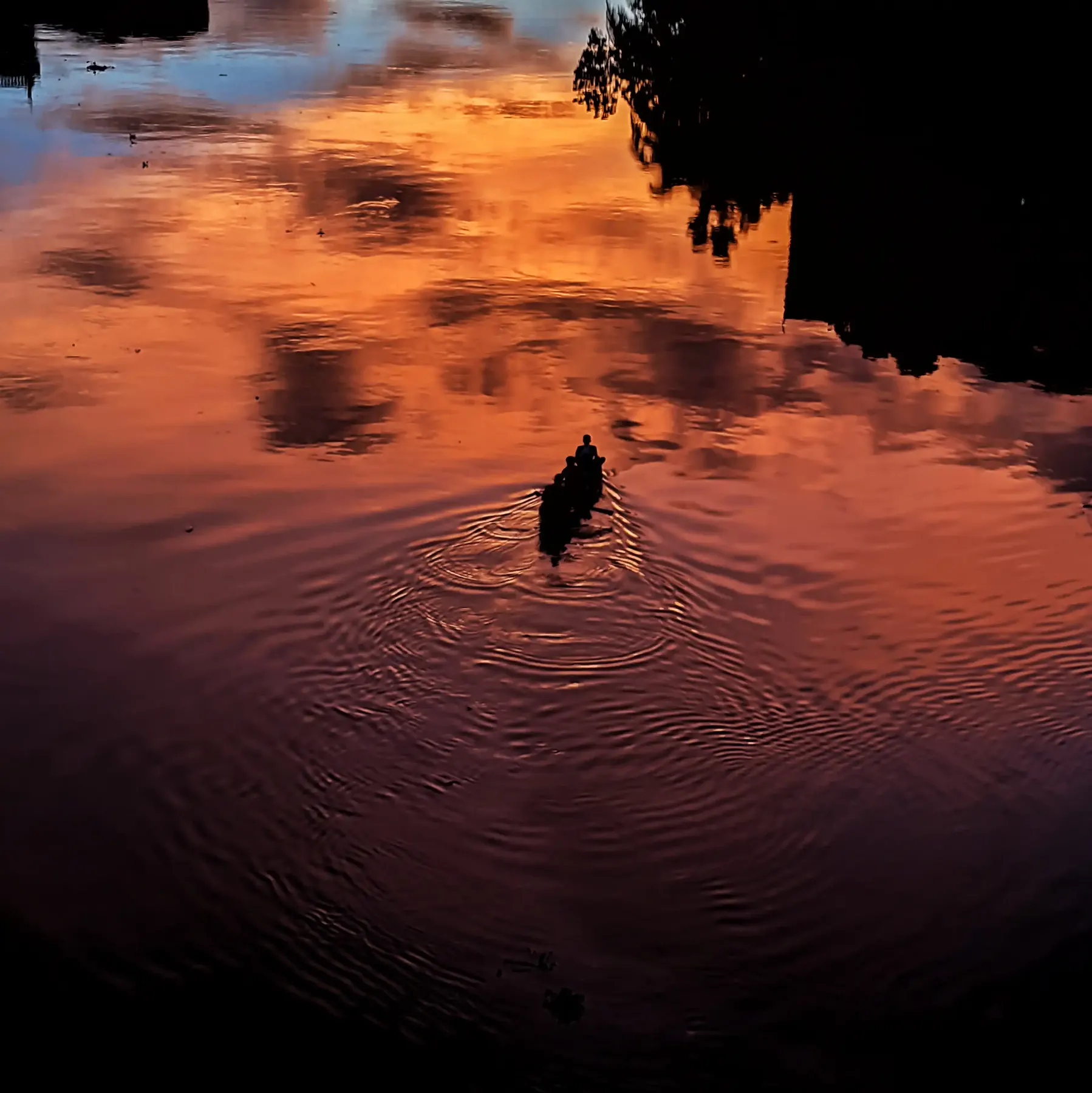 A person wading through reflective orange river water at sunset